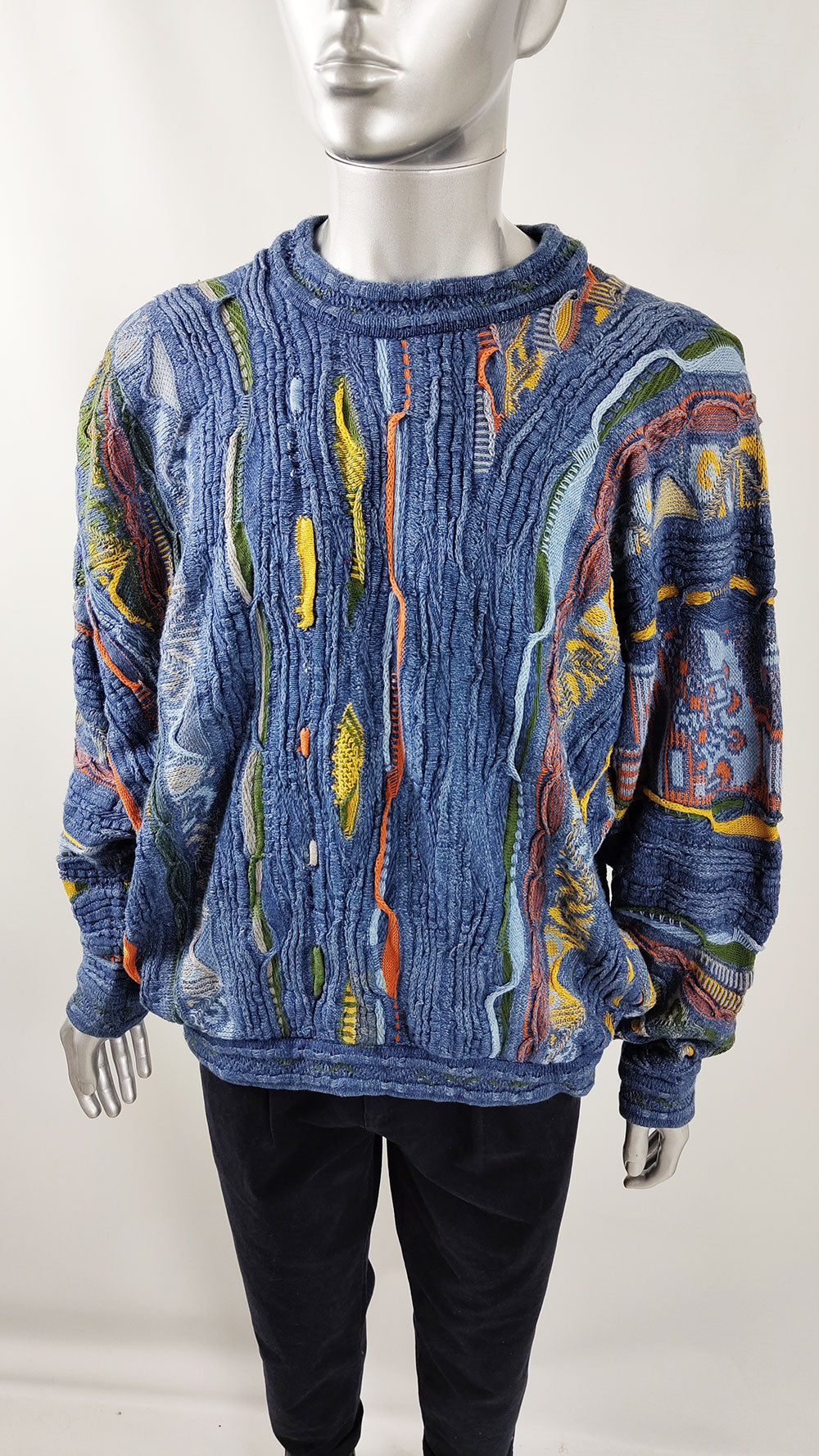 A male mannequin wearing a vintage Coogi sweater in a blue texture knit.