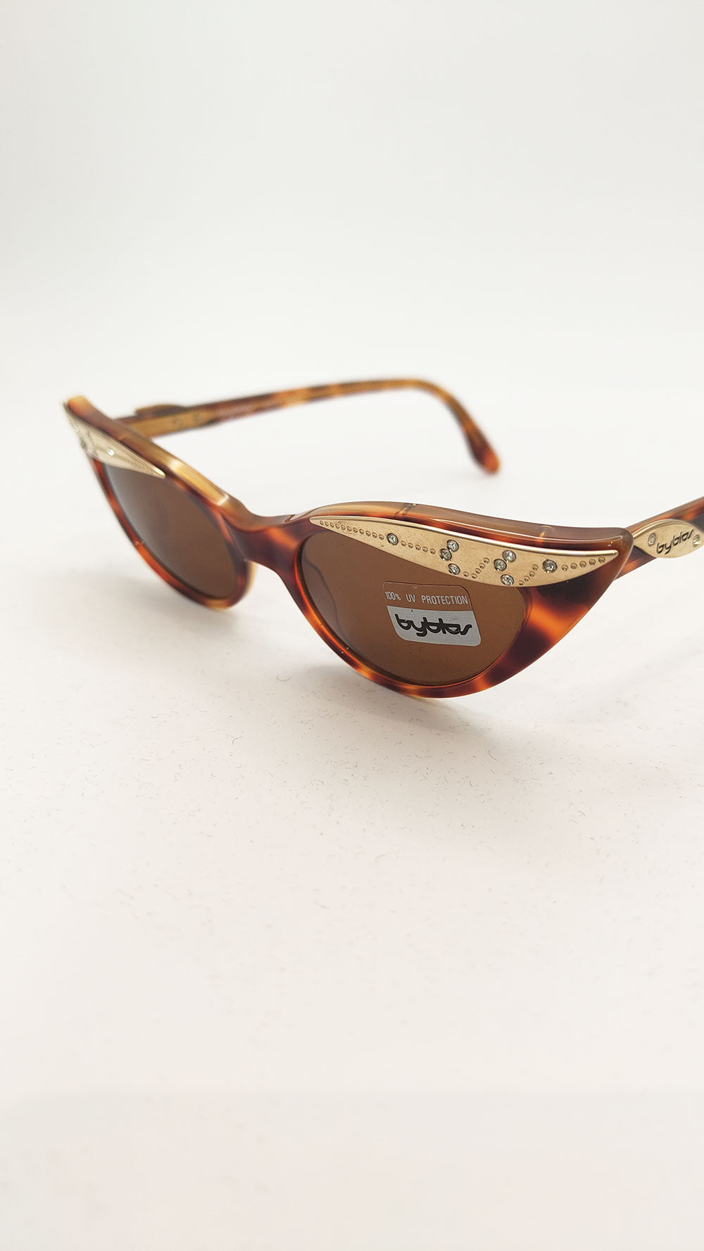 A vintage pair of womens sunglasses by luxury fashion house, Byblos. Made from a tortoiseshell patterned plastic with gold tone hardware and rhinestone detailing.