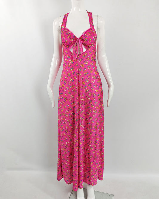 A vintage 1970s maxi dress in a pink fabric with a ditsy floral print throughout with cut outs at the waist and a halter neck design.